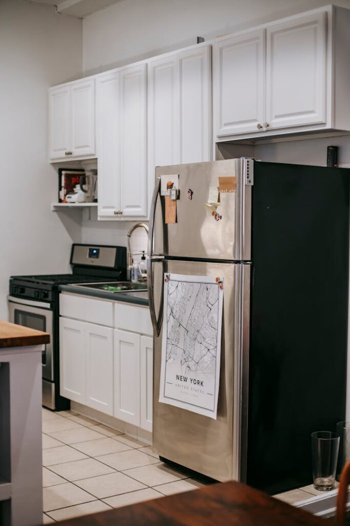 Modern light kitchen furnished with refrigerator and white cupboards placed near stove oven in modern cozy apartment with tiled floor